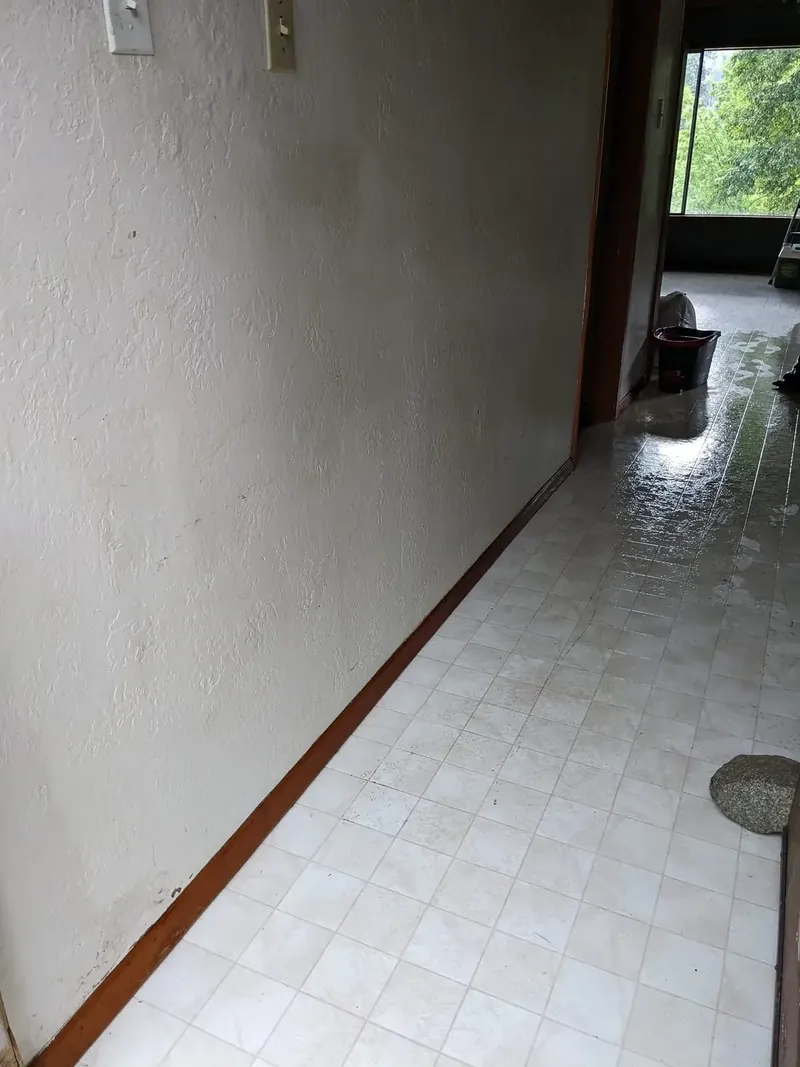 Bright interior hallway after cleaning, with mopped tile flooring reflecting daylight from the room beyond.