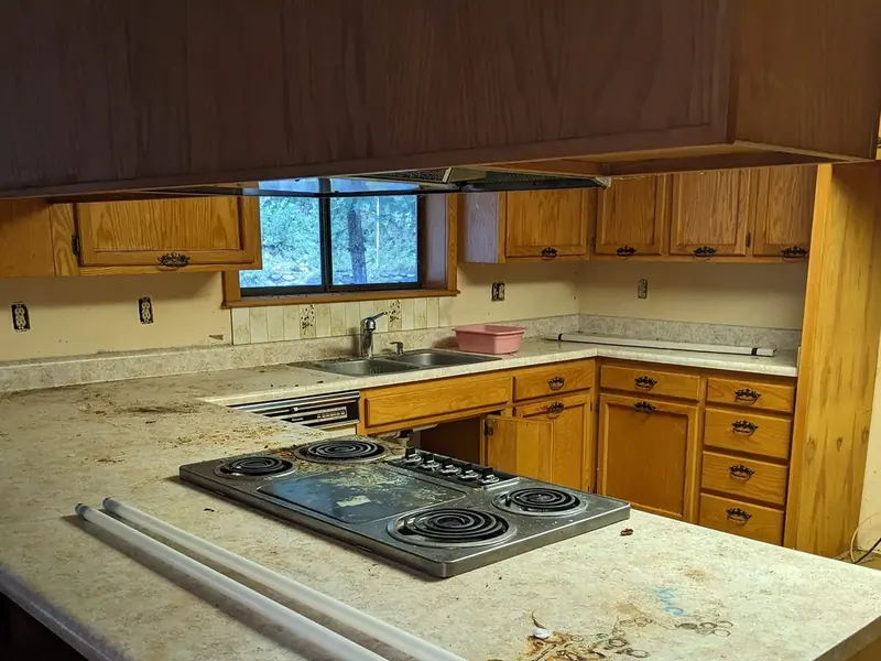 Kitchen before cleaning, with debris scattered across the laminate counters and a heavily soiled downdraft cooktop.